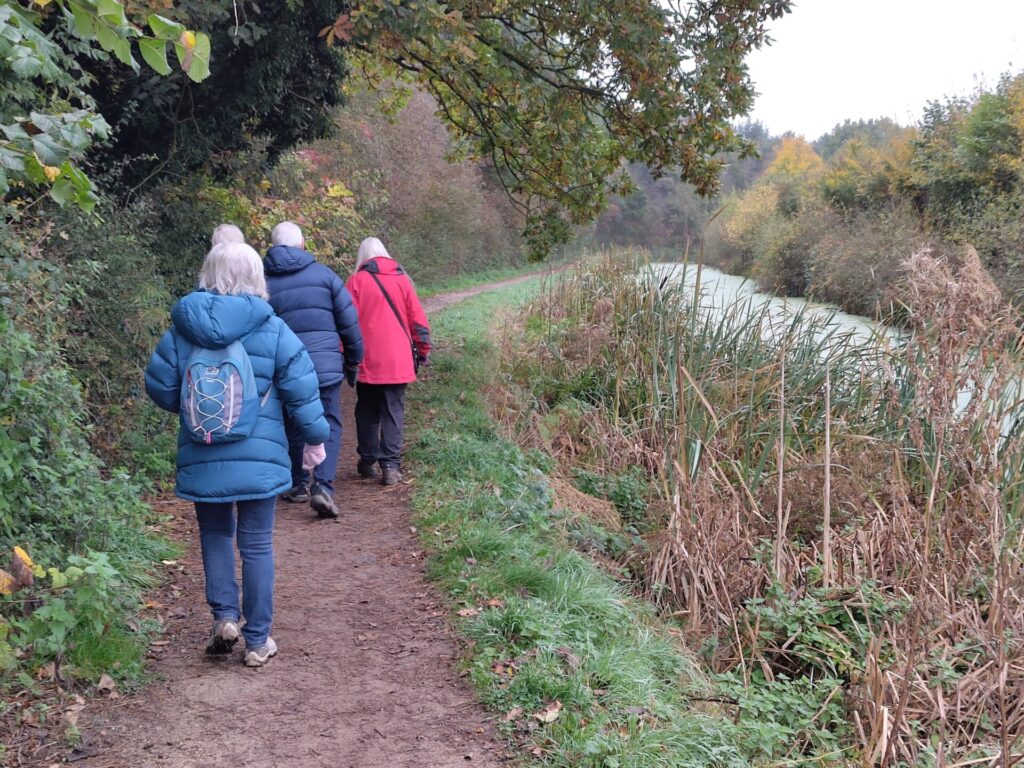 Back view of four people walking alongside Cossall Canal amid trees and vegetation