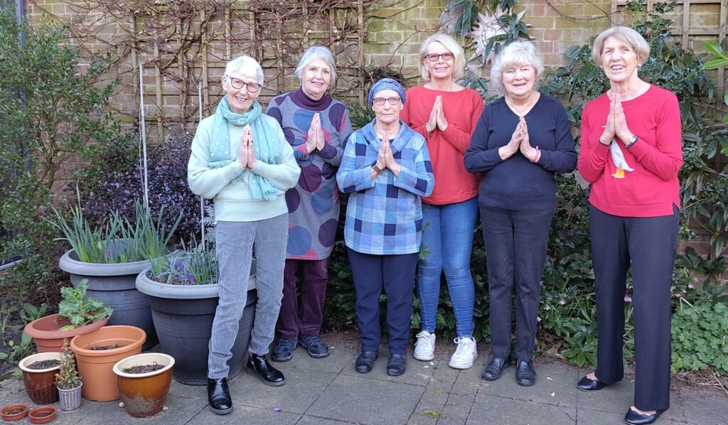 Exploring Meditation group members making namaste gesture (palms touching and fingers pointing upwards) in library courtyard garden.