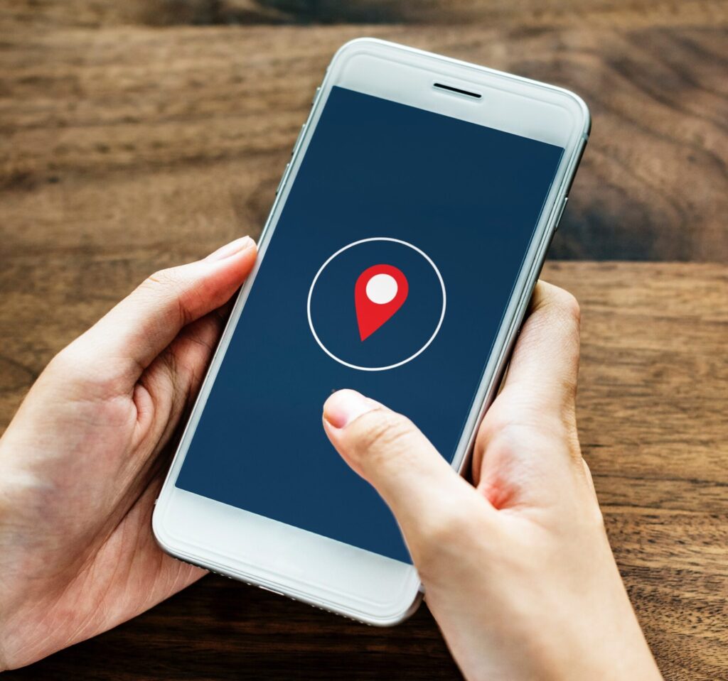 A pair of hands holding a smartphone with a red location-pin symbol on the screen.